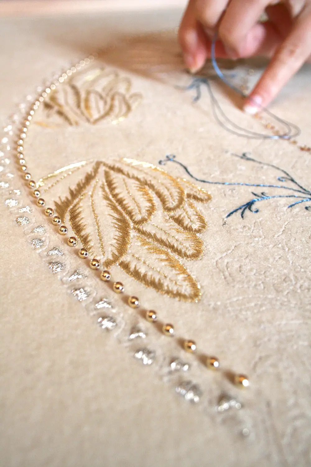Le travail de la brodeuse Photo issue du reportage réalisé par Luce Dupont, dans l'atelier de la brodeuse. Au premier plan, des broderies mêlant perles et fils d'or avec la main au travail en fond d'image. Photo Via tara